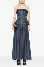 Woman wearing a navy blue denim maxi dress with a ruffled strapless neckline and peplum waist