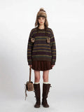 Woman wearing a striped knit sweater with faux fur pom-poms, a brown corduroy pleated skirt, white knee-high socks, brown leather boots, and a matching faux fur hat with ear flaps.