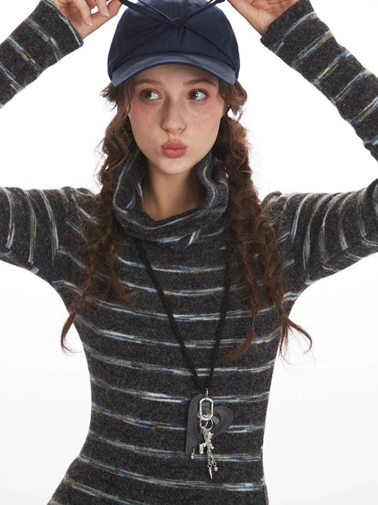 Front view of a model in a striped turtleneck sweater and pleated skirt, wearing a navy blue baseball cap and a necklace.