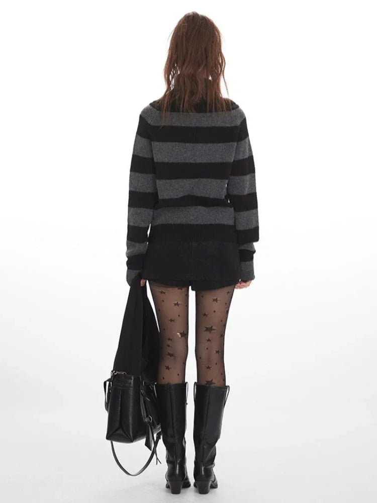 Rear view of a woman wearing a grey and black striped knit sweater with a cowl neck, black shorts, black patterned tights, and black boots, holding a black handbag.