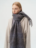 Close-up of the plaid pattern and fringed edge of a wool blend scarf.