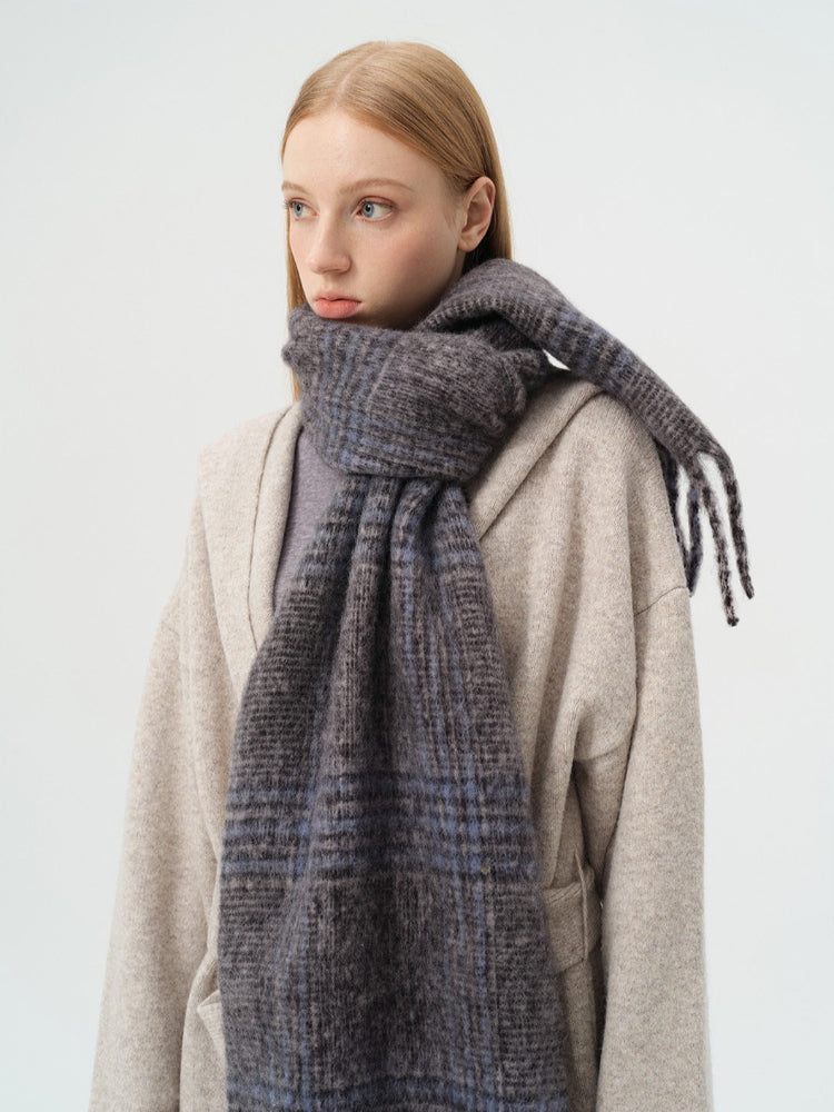 Close-up of the plaid pattern and fringed edge of a wool blend scarf.