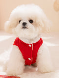 Small white dog wearing a red corduroy dog vest with white buttons and faux fur trim.