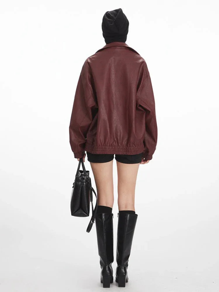 Woman wearing a burgundy faux leather bomber jacket with a black beanie and black shorts