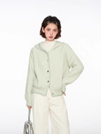 Woman wearing a light green hooded cardigan with a white top and cream wide-leg pants, holding a silver handbag.