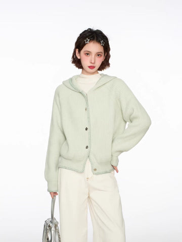 Woman wearing a light green hooded cardigan with a white top and cream wide-leg pants, holding a silver handbag.