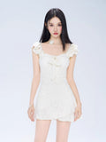 Woman wearing a white jacquard fit and flare mini dress with ruffled cap sleeves and a sweetheart neckline with a bow detail.