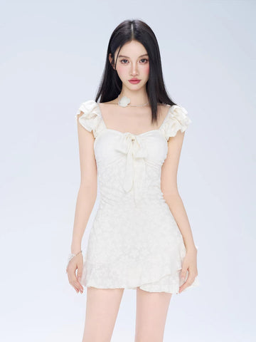 Woman wearing a white jacquard fit and flare mini dress with ruffled cap sleeves and a sweetheart neckline with a bow detail.