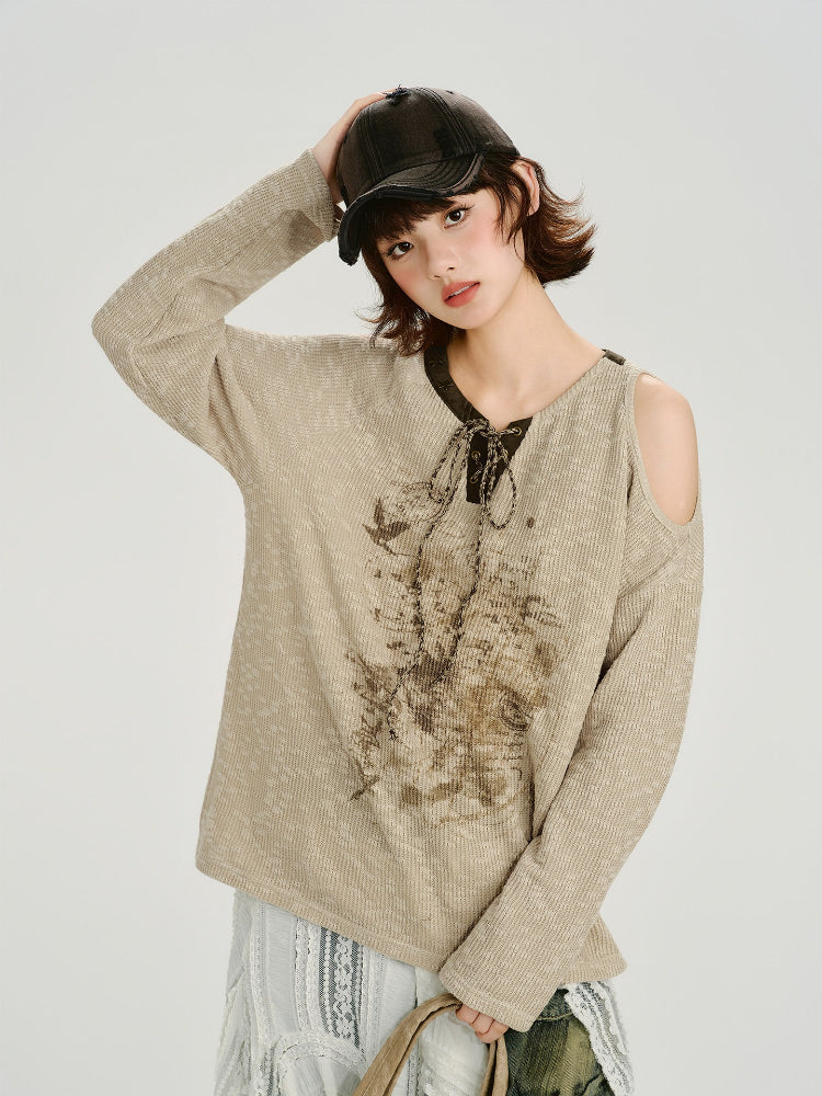 Woman wearing a beige knit sweater with a graphic print and cold shoulder detail.