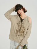 Woman wearing a beige knit sweater with a graphic print and cold shoulder detail.