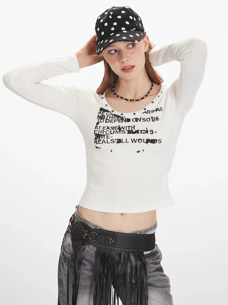Close-up of a woman wearing a white long-sleeve graphic t-shirt with a scoop neckline and studded details.