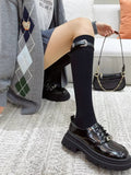 Close-up of a woman's legs in black knee-high socks with a buckle strap, paired with a grey argyle cardigan and black platform loafers.