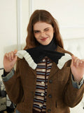 Woman wearing a brown plaid textured jacket and a striped knit top, adjusting a black scarf with white ruffled ends.