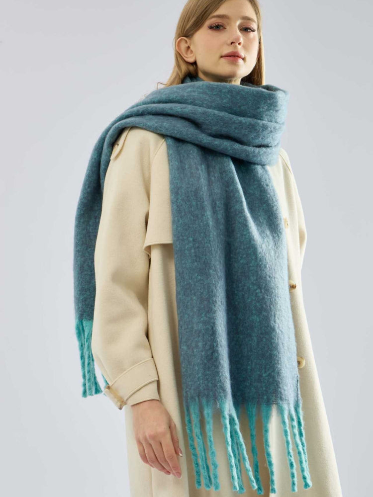 Woman wearing a teal oversized scarf with fringe detail over a cream coat.