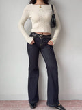Woman wearing a cream cable knit cropped sweater with dark wash flare jeans and a black belt
