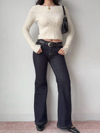 Woman wearing a cream cable knit cropped sweater with dark wash flare jeans and a black belt