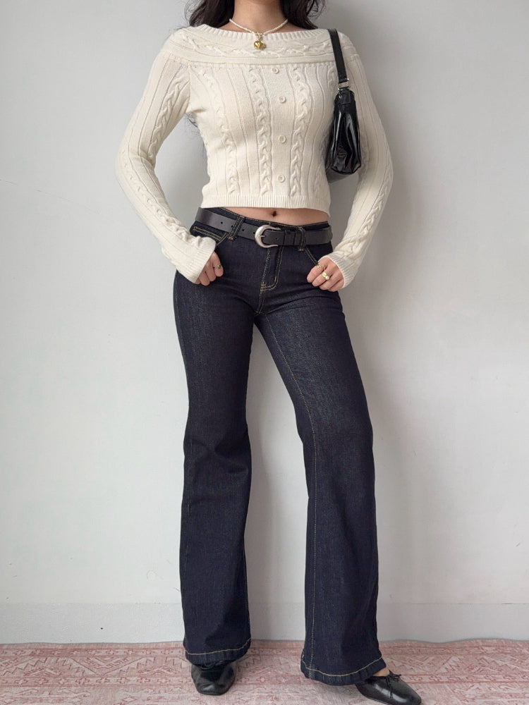 Woman wearing a cream cable knit cropped sweater with dark wash flare jeans and a black belt