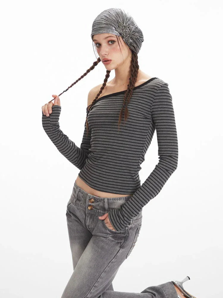 Woman posing in a grey and black striped off-the-shoulder long sleeve top and grey wash jeans, touching her braid.