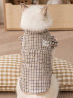 Back view of a cat wearing a brown plaid pet vest with ruffled sleeves and a leash ring.
