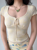 Close-up of a woman wearing a yellow sheer mesh top with a floral pattern and a drawstring tie at the neckline.