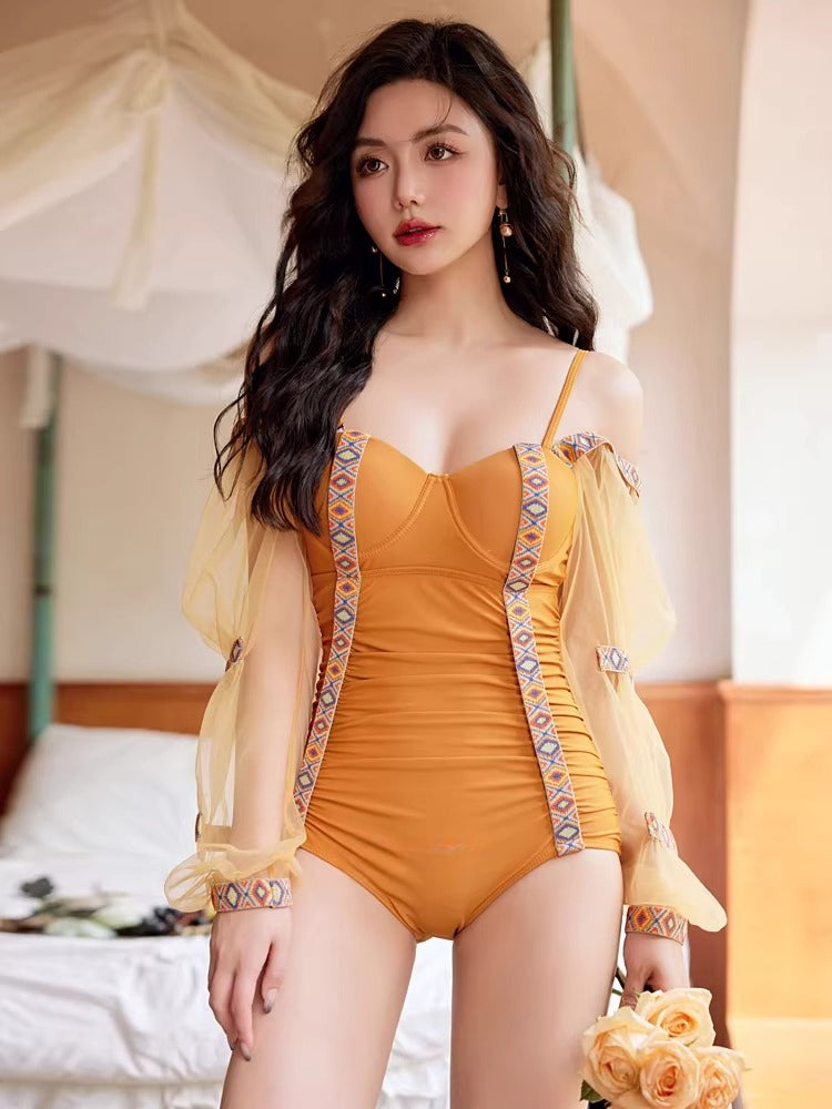 Model posing in a mustard yellow swimsuit with off-the-shoulder sheer sleeves