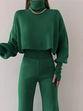 Woman wearing a green knit turtleneck crop top with balloon sleeves and matching green knit pants.