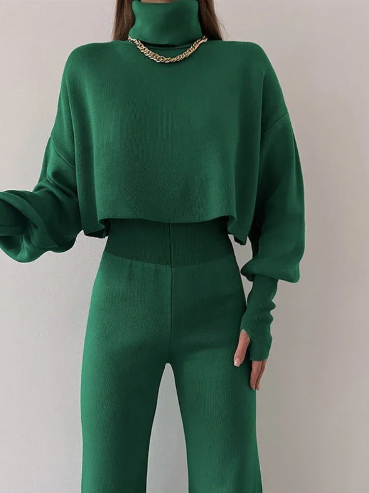 Woman wearing a green knit turtleneck crop top with balloon sleeves and matching green knit pants.