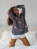 Woman wearing a grey knit sweater with a red and white mushroom print, hands behind her head.