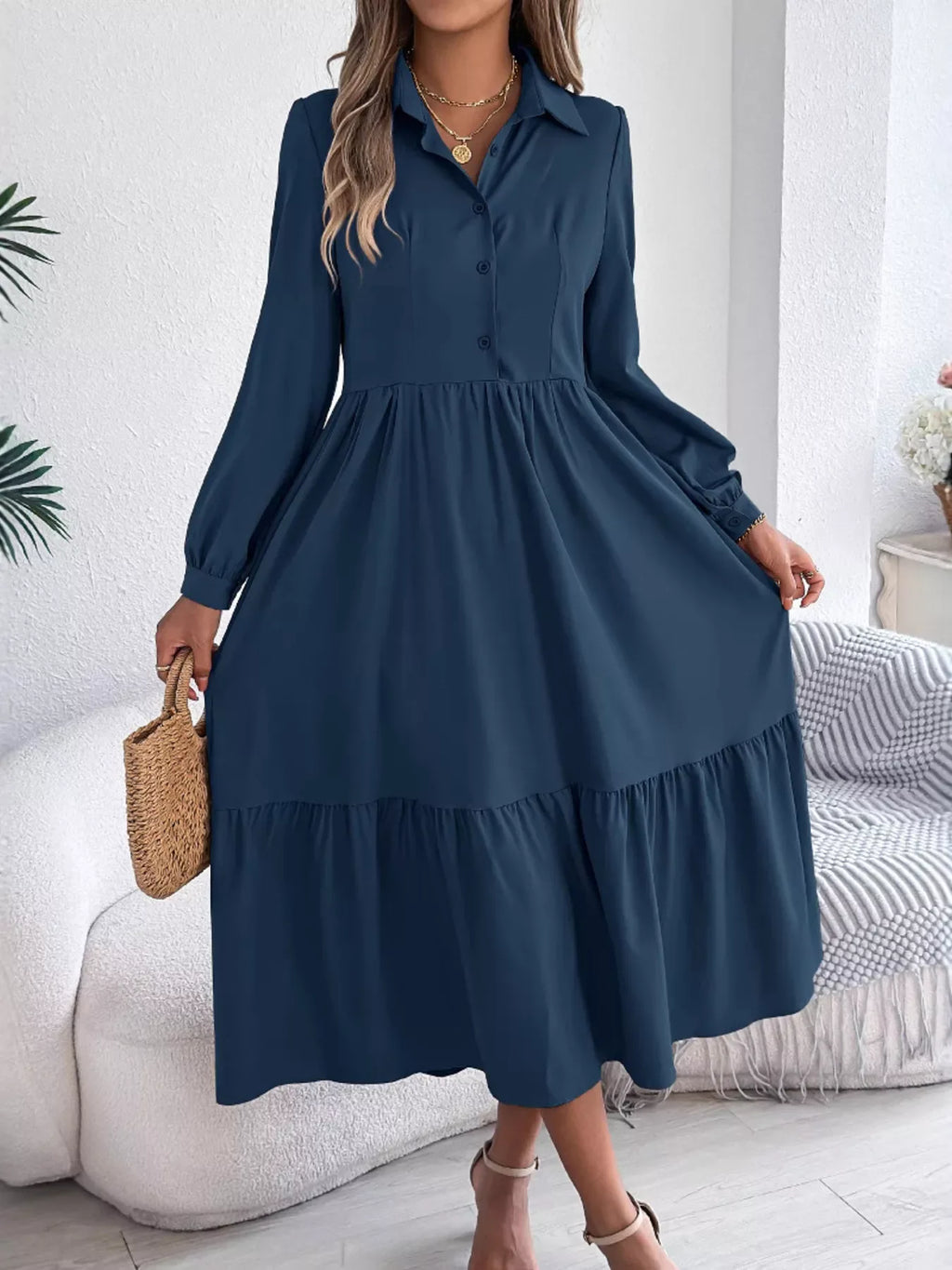Woman wearing a long-sleeved, collared, navy blue midi dress with a tiered hem and button-down front.