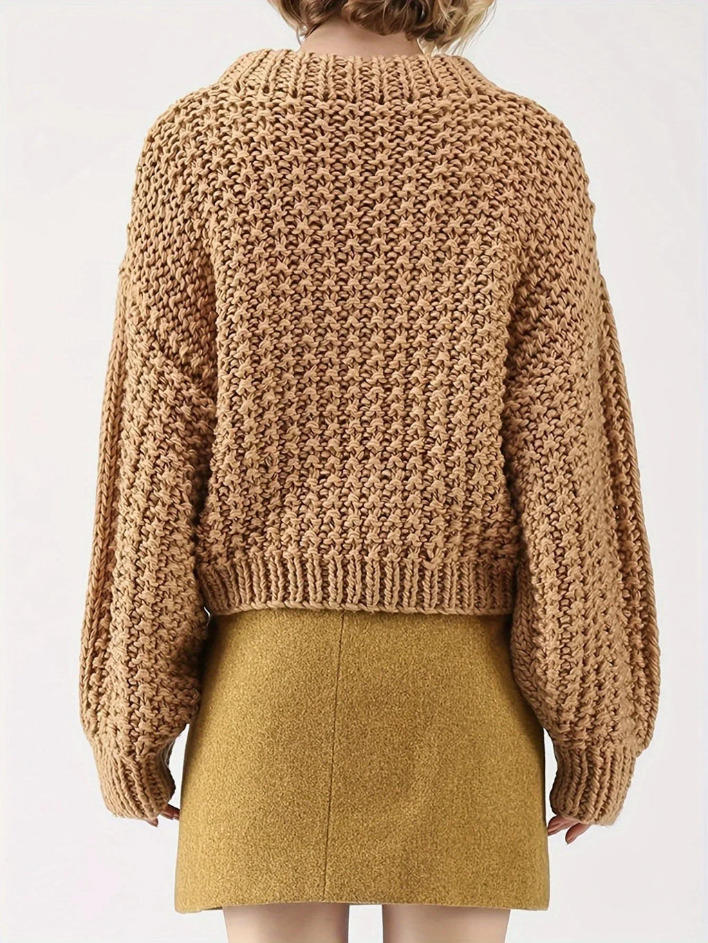Back view of a woman in a tan chunky knit sweater with balloon sleeves and a mock neckline.