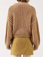 Back view of a woman in a tan chunky knit sweater with balloon sleeves and a mock neckline.