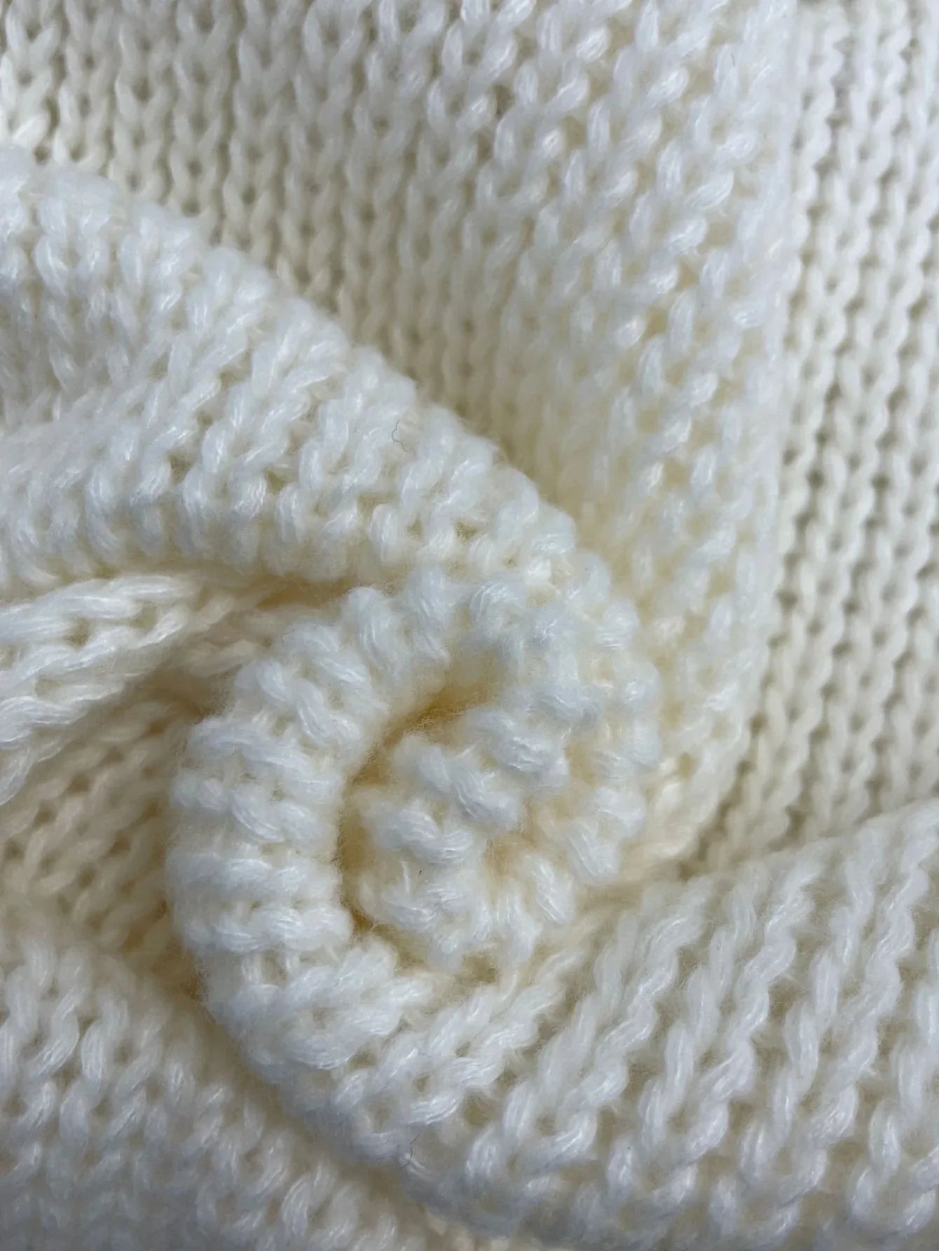 Detail of the V-neck and wrap front of a cream chunky knit sweater.