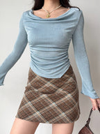 Woman wearing a light blue long-sleeve top with a cowl neckline and ruched side detail.