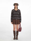 Woman wearing a brown striped V-neck knit sweater with a pleated mini skirt and knee-high boots.