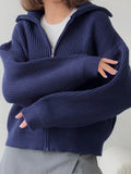 Woman showing the sleeve detail of a navy blue oversized knit jacket.