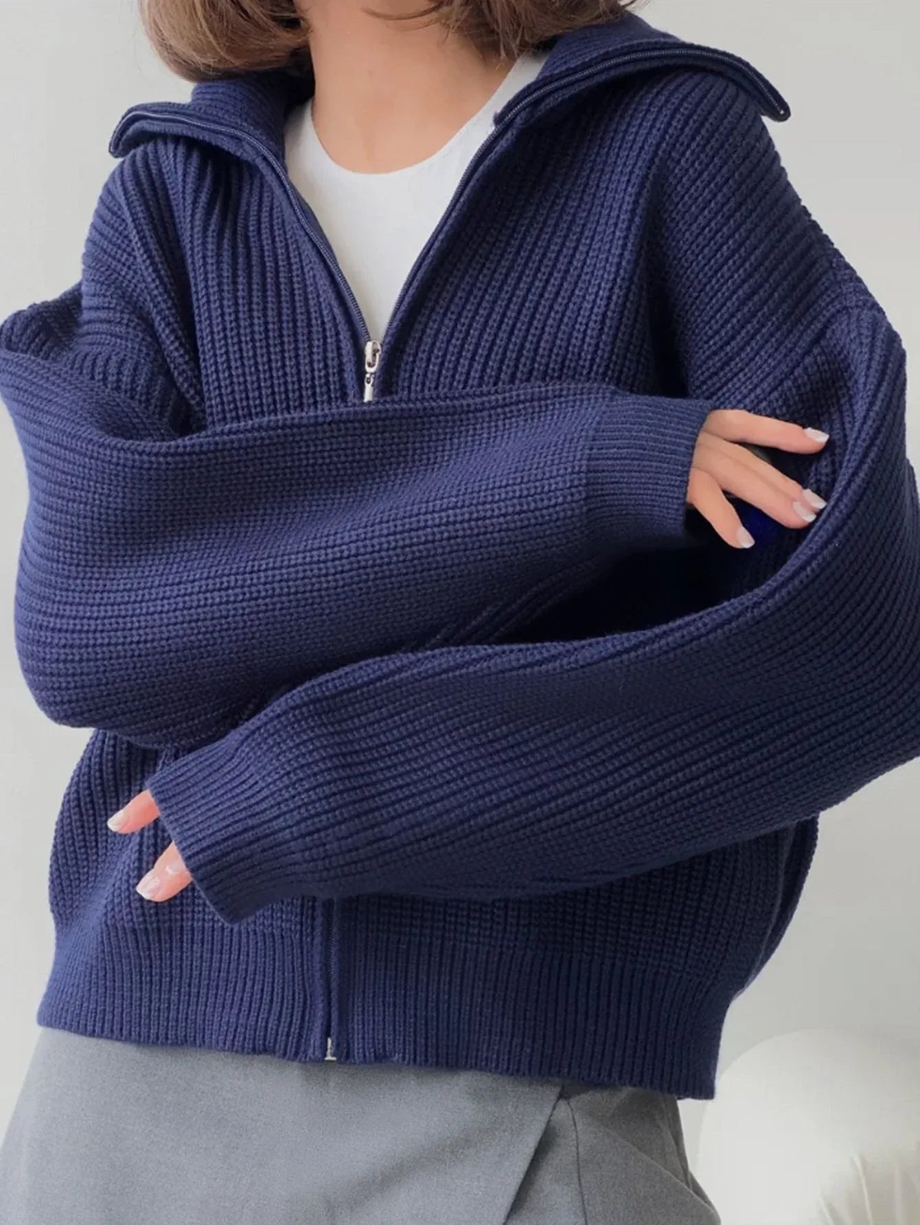 Woman showing the sleeve detail of a navy blue oversized knit jacket.