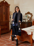 Woman wearing a navy knit sweater with gray and navy horizontal stripes and snowman embellishments on the scarf.
