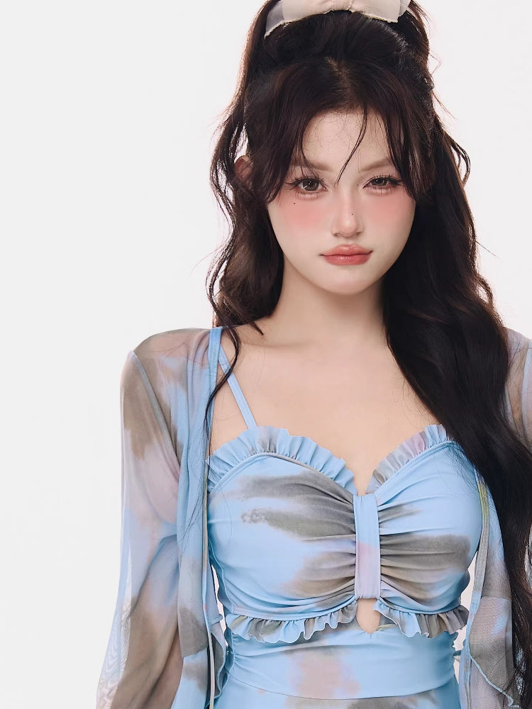 Close-up of a woman's chest area showing the blue abstract print and ruffled neckline of the dress