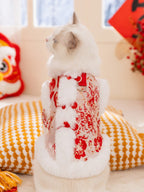Rear view of a white cat wearing a red traditional Chinese style coat with a red floral print and faux fur trim, showing the leash attachment ring