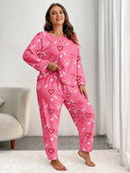 Woman wearing a pink long-sleeved pajama set with an all-over heart print, standing and adjusting her top.