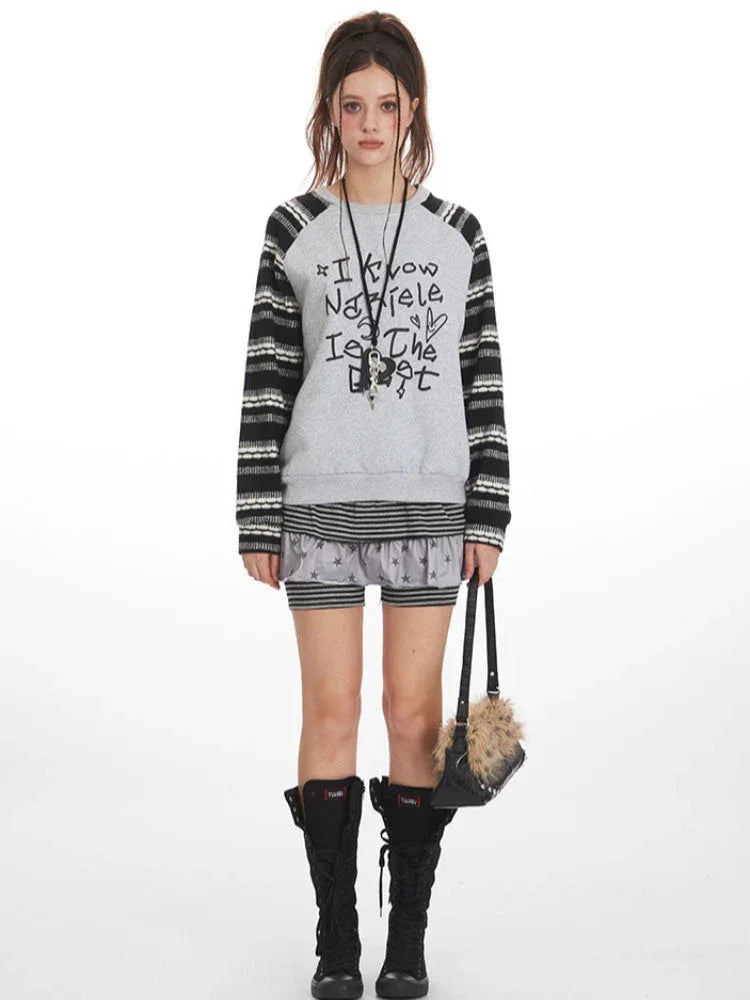 Model wearing a grey graphic print sweatshirt with striped sleeves and shorts.