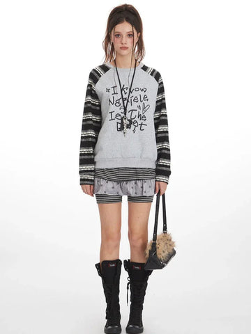 Model wearing a grey graphic print sweatshirt with striped sleeves and shorts.