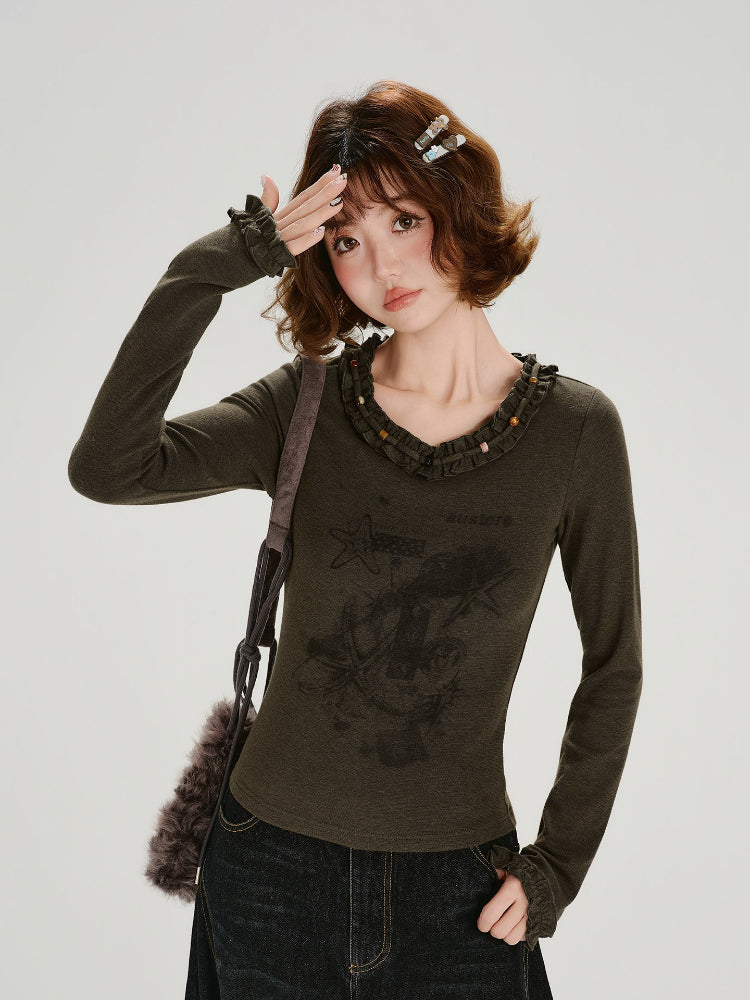 Woman wearing a dark olive long-sleeve graphic t-shirt with ruffled neckline and cuffs.
