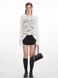 Woman wearing a white long-sleeve sheer knit t-shirt with a black dog graphic print and text, paired with black shorts and black knee-high socks.