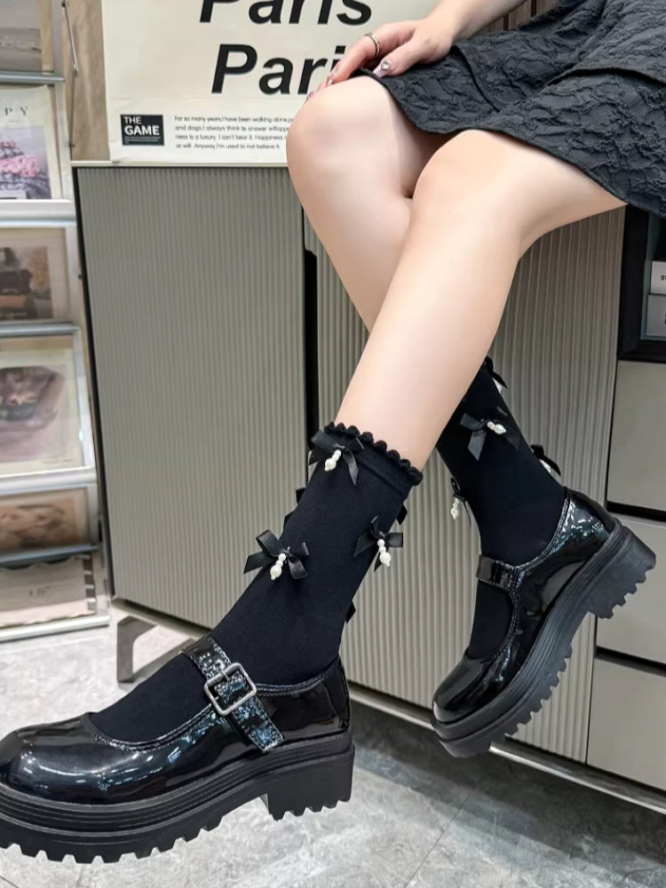 View of black ankle socks with ruffled trim and bow details, paired with black platform mary jane shoes, styled with a black skirt