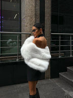 Woman sitting on stairs wearing a cream faux fur cropped jacket and grey trousers.