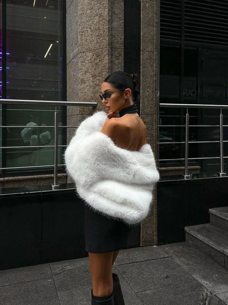 Woman sitting on stairs wearing a cream faux fur cropped jacket and grey trousers.