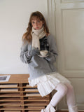 Woman in a grey sweatshirt and white skirt holding a teacup