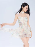 Woman posing in a flowing floral print mini dress with asymmetrical overlay
