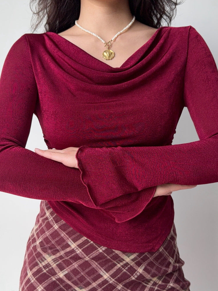 Close-up of a woman wearing a burgundy long-sleeve top with a cowl neckline and ruched side detail.